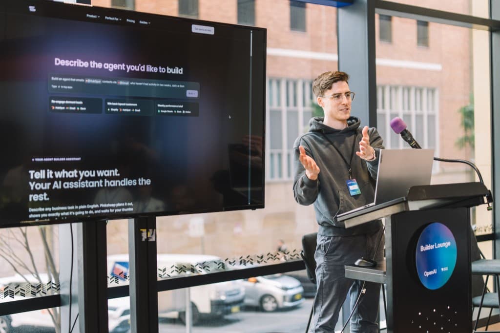 Nick Hugh presenting Pinksheep at the OpenAI Builder Lounge in Sydney, with the Pinksheep landing page on screen and Builder Lounge signage on the podium.